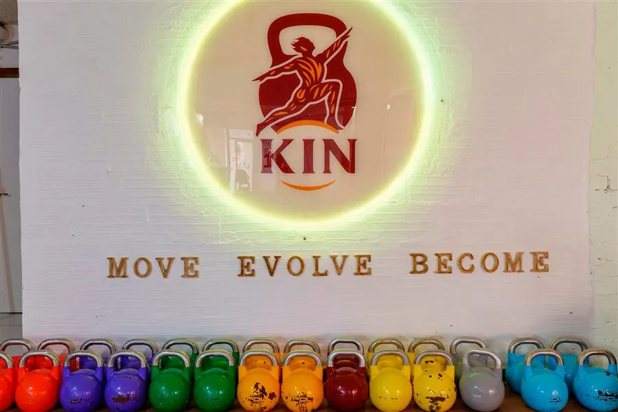 Logo de KIN Studio en neón con el lema move, evolve, become sobre una fila de kettlebells